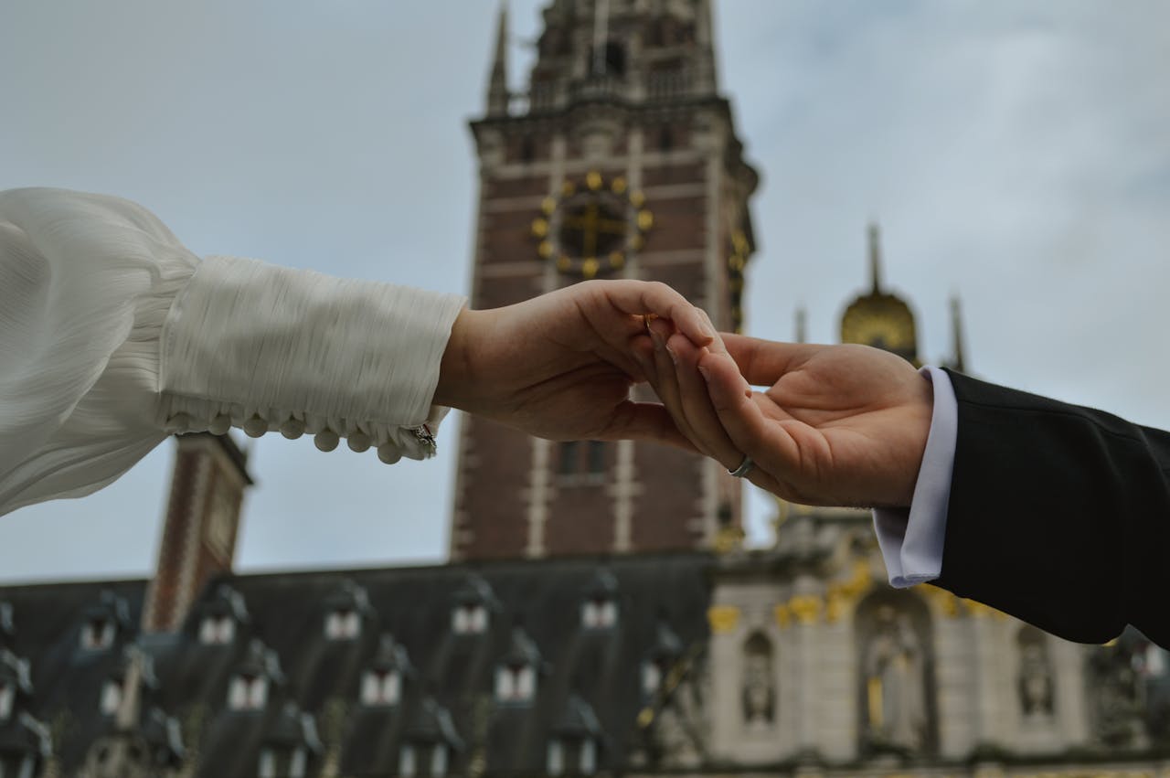 A romantic moment between a couple holding hands in front of a historic church tower.