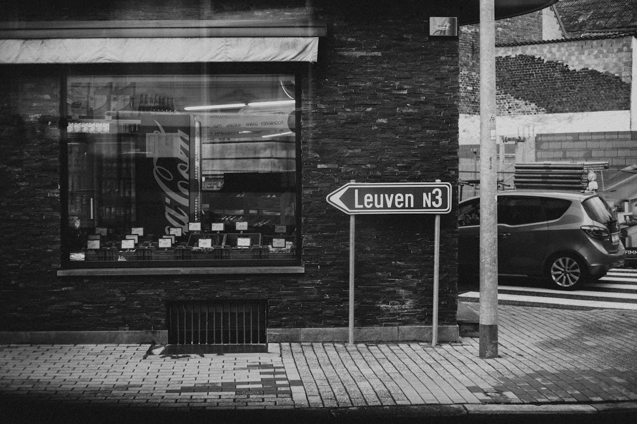 Black and white of shop in building on pavement and automobile on asphalt road